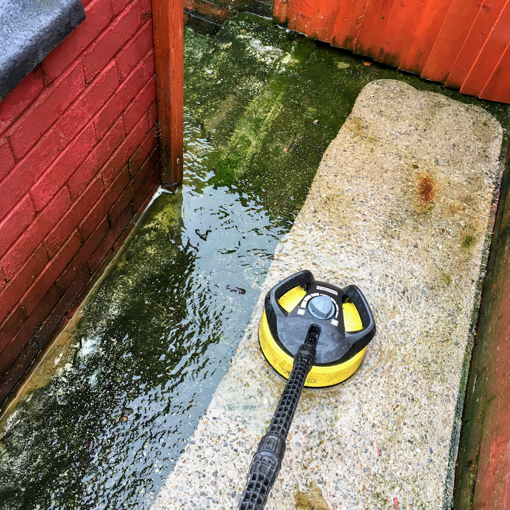 Rotary patio cleaner lifting algae from concrete slabs